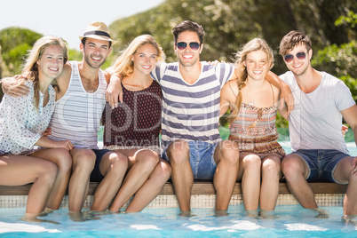 Group of friends sitting side by side at poolside