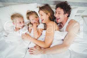 High angle view of smiling family enjoying on bed