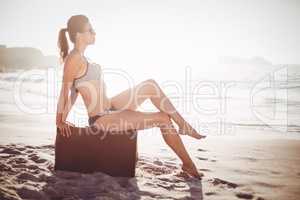 Glamorous woman in bikini sitting on an old suitcase