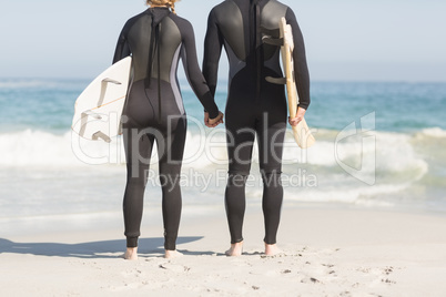 Rear view of couple with surfboard holding hands on the beach