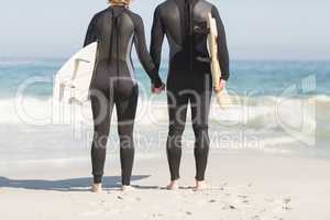 Rear view of couple with surfboard holding hands on the beach
