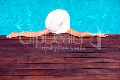 Woman wearing hat leaning on wooden deck by poolside