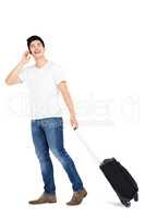 Young man talking on mobile phone while walking with suitcase