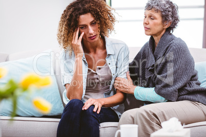 Mother comforting sad daughter sitting on sofa