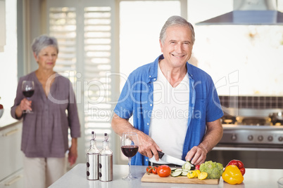 Portrait of senior man cutting vegetables with wife in backgroun