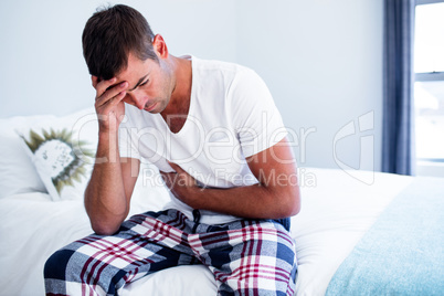 Young man sitting with stomach pain on bed
