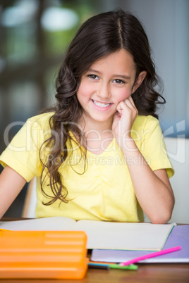 Happy girl with hand on chin while sitting at desk
