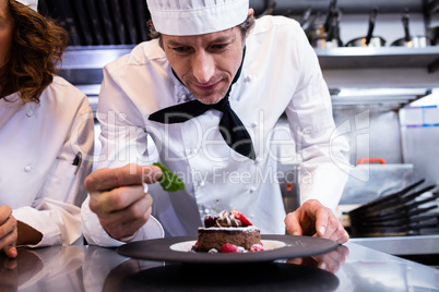 Male chef garnishing his dessert with a mint leaf on counter