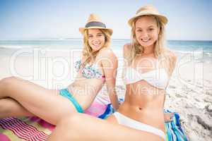 Pretty women in bikini and beach hat sitting on the beach