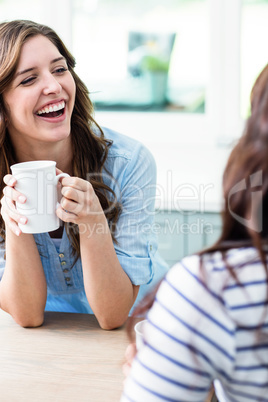 Cheerful friends holding coffee mugs while sitting at table