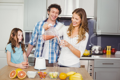 Smiling mother pouring fruit juice in glass with family