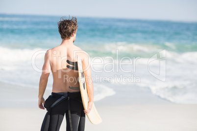 Rear view of man with surfboard standing on the beach
