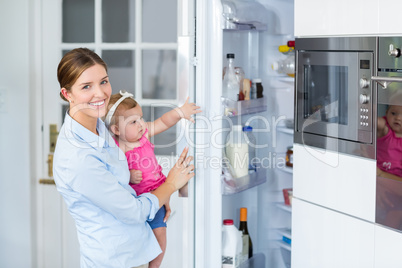 Woman opening refrigerator while carrying baby girl