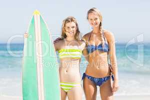 Portrait of two women in bikini standing with a surfboard on the