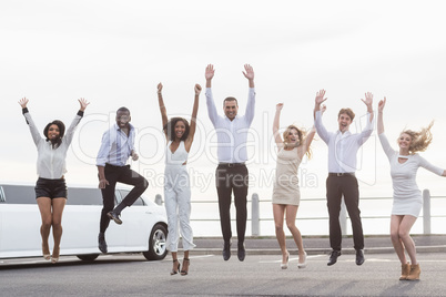 Well dressed people jumping next to a limousine