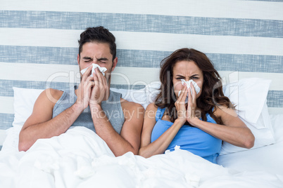 Young couple covering nose while sneezing on bed