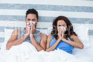 Young couple covering nose while sneezing on bed