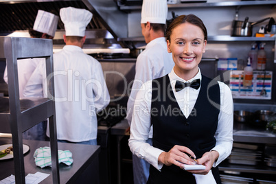 Smiling waitress with note pad in commercial kitchen