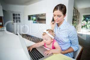 Woman using mobile phone and baby girl playing with laptop