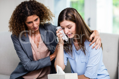 Female psychologist consoling depressed woman on sofa at home