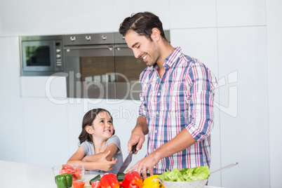 Smiling father cutting vegetables with daughter