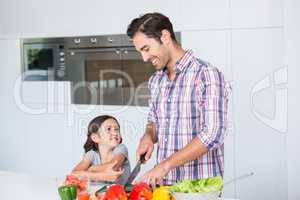 Smiling father cutting vegetables with daughter