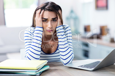 Tensed woman with head in hands sitting with laptop