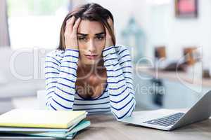 Tensed woman with head in hands sitting with laptop