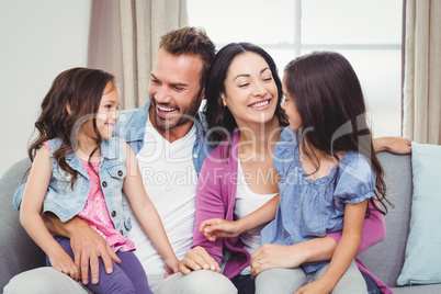 Parents smiling while sitting with daughters on sofa