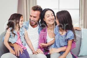 Parents smiling while sitting with daughters on sofa