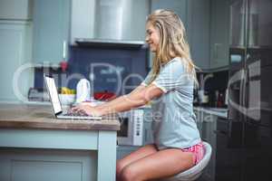 Happy beautiful woman using laptop at table in kitchen