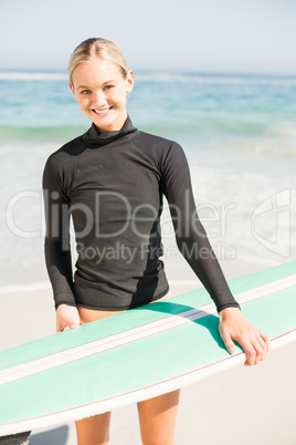 Woman in wetsuit holding a surfboard on the beach