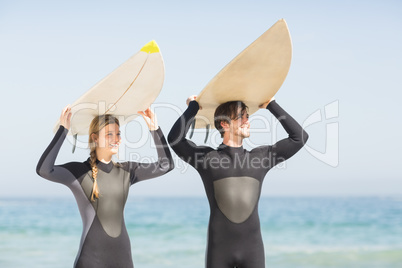 Happy couple in wetsuit carrying surfboard over head
