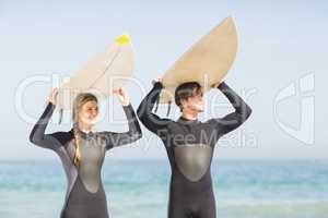 Happy couple in wetsuit carrying surfboard over head