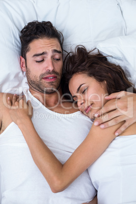Irritated man looking at woman relaxing on bed