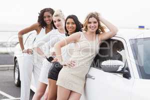 Well dressed women posing leaning on a limousine