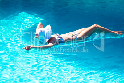 Woman wearing bikini and hat lying on air bed in pool