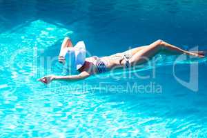 Woman wearing bikini and hat lying on air bed in pool