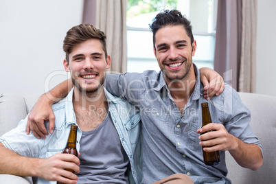 Happy young male friends enjoying beer while sitting on sofa