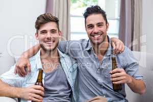 Happy young male friends enjoying beer while sitting on sofa