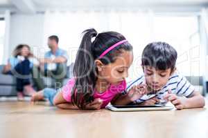Brother and sister lying on floor and using digital tablet