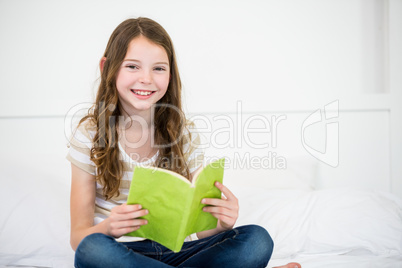 Cute happy girl reading book on bed