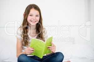 Cute happy girl reading book on bed