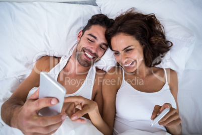 High angle view of happy couple using smartphone on bed High angle view of happy couple using smartphone on bed