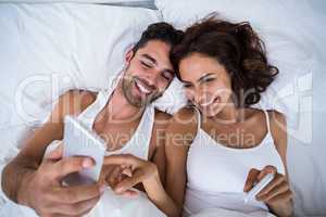High angle view of happy couple using smartphone on bed