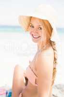 Pretty woman in bikini and beach hat sitting on the beach