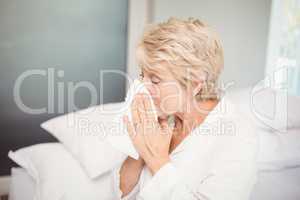 Senior woman covering nose while sneezing at home