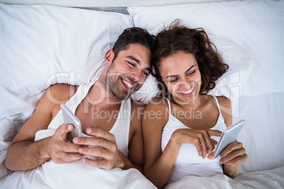 High angle view of smiling couple using smartphone on bed