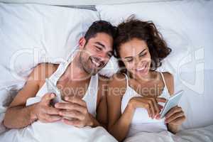 High angle view of smiling couple using smartphone on bed