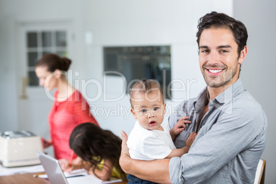 Portrait of smiling father carrying baby at home